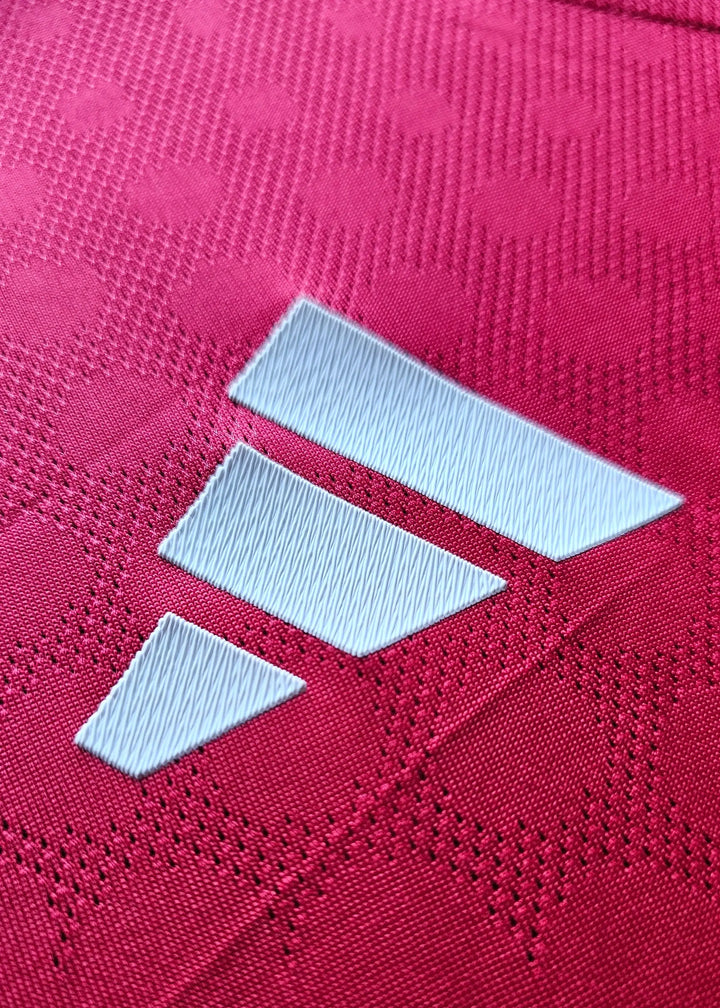 Close-up view of the adidas logo in white on a red football shirt.