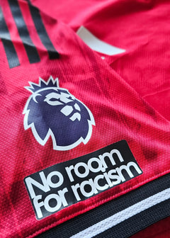 Close-up of Manchester United crest and 'No room for racism' text on red football shirt.