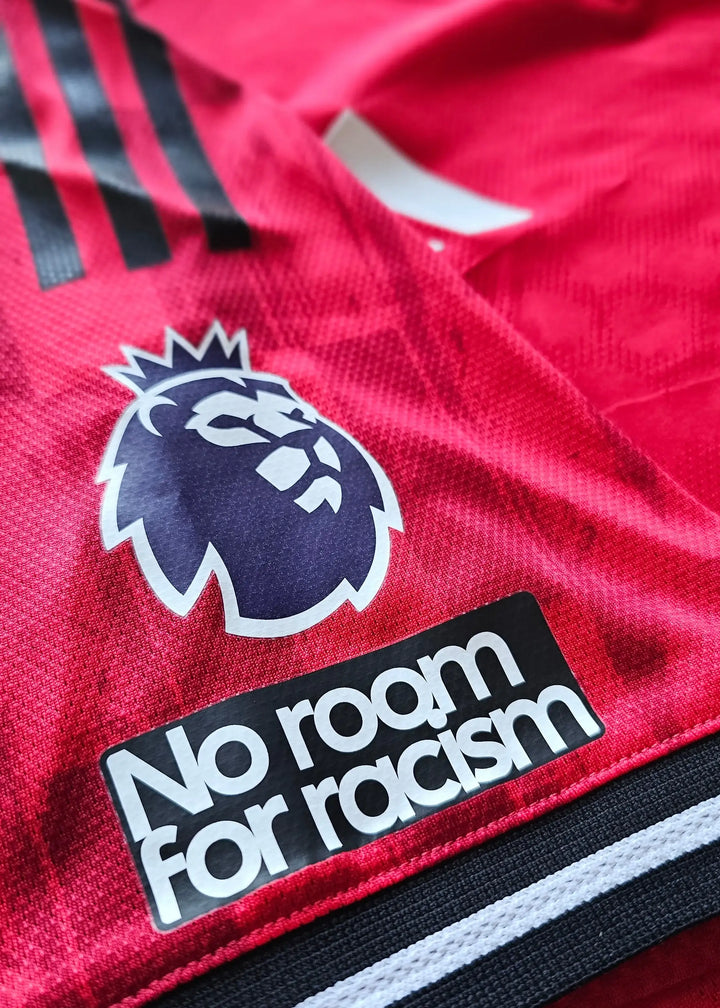 Close-up of Manchester United crest and 'No room for racism' text on red football shirt.