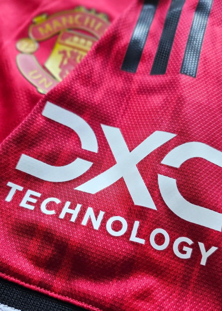 Close-up of Manchester United crest and CX Technology sponsor on red football shirt.