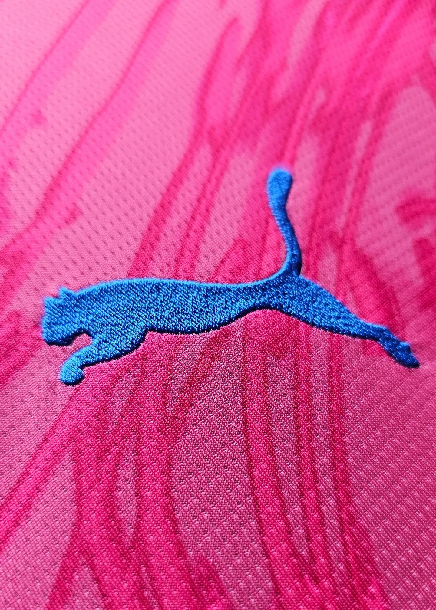 Close-up of blue Puma logo embroidered on pink fabric with a textured pattern.