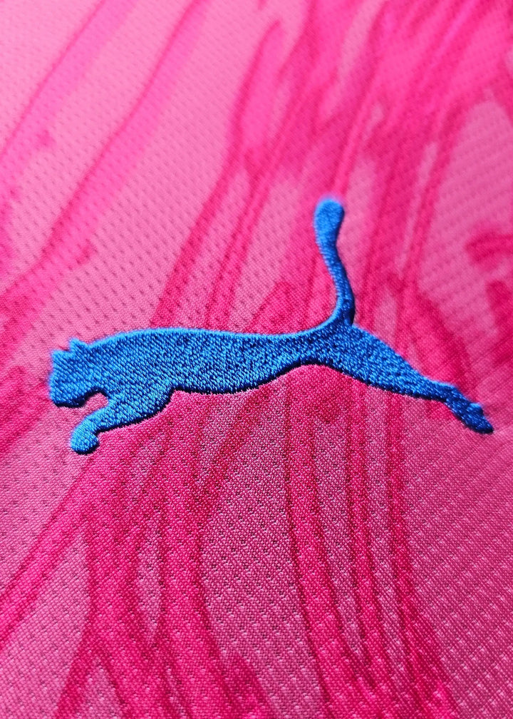 Close-up of blue Puma logo embroidered on pink fabric with a textured pattern.
