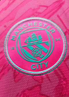 Crest of Manchester City with ship logo and 'MAN CITY' text on a pink background.