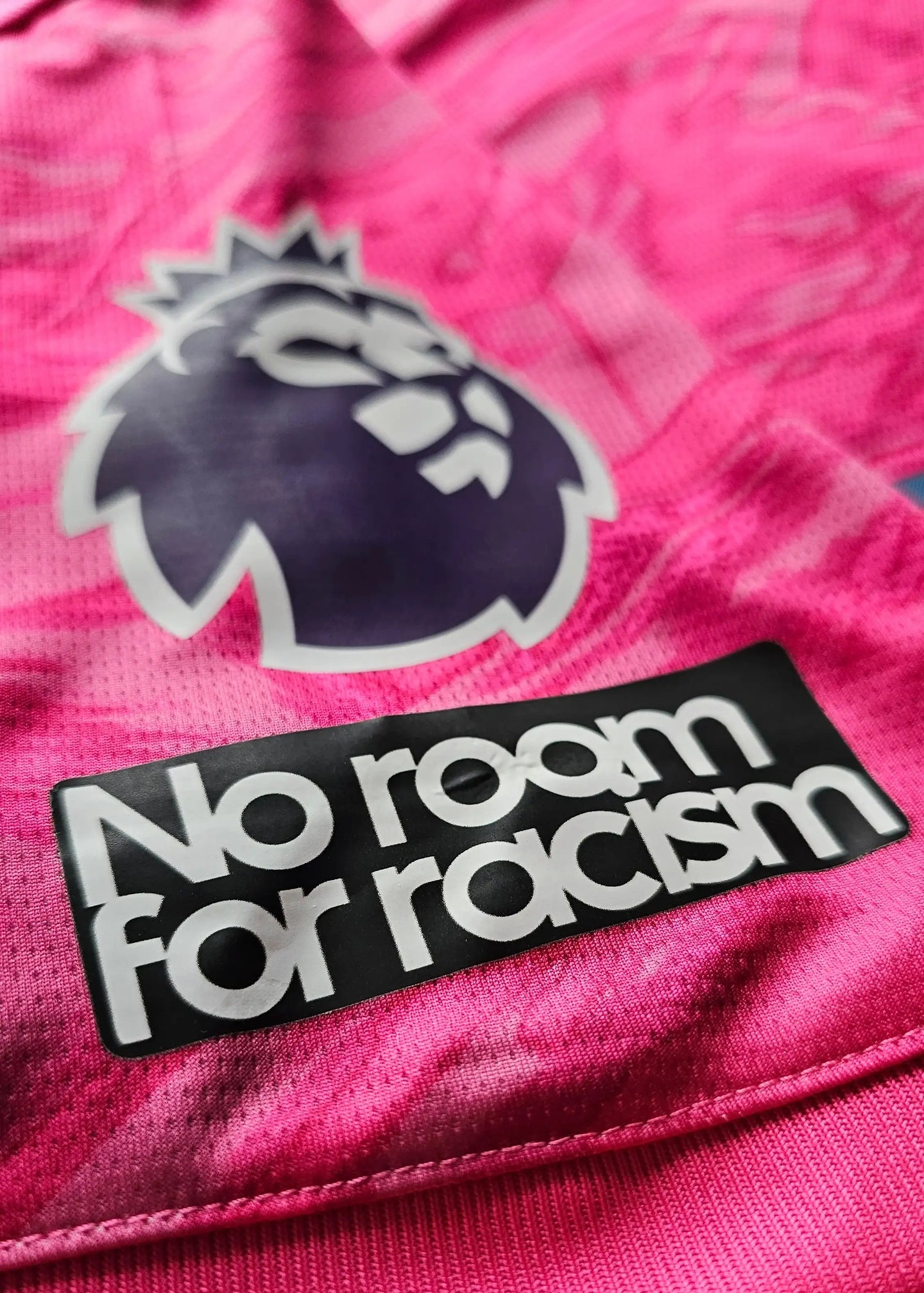 Close-up of the Premier League lion crest and 'No room for racism' on a pink football shirt.