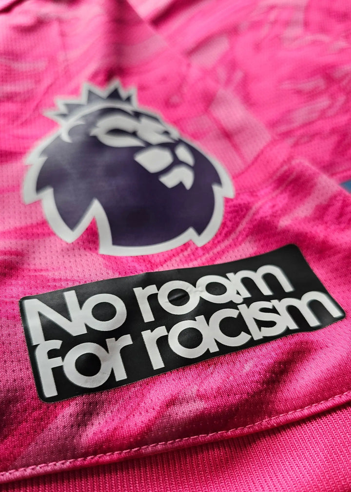 Close-up of the Premier League lion crest and 'No room for racism' on a pink football shirt.