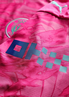 Crest detail featuring Manchester City badge and visible sponsor logo on a pink football shirt.