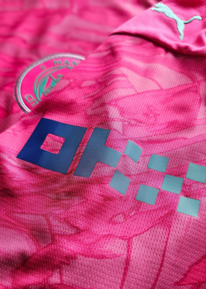 Crest detail featuring Manchester City badge and visible sponsor logo on a pink football shirt.