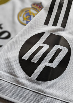 Close-up detail showing Real Madrid crest and HP sponsor logo on a white football shirt.
