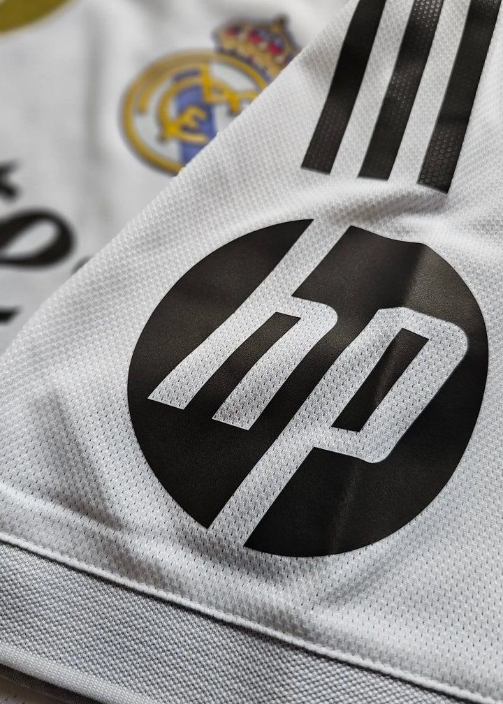 Close-up detail showing Real Madrid crest and HP sponsor logo on a white football shirt.