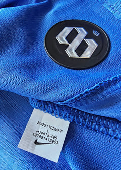 Detail of blue football shirt showing Nike tag and black crest with silver emblem.