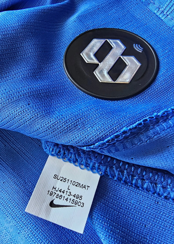 Detail of blue football shirt showing Nike tag and black crest with silver emblem.