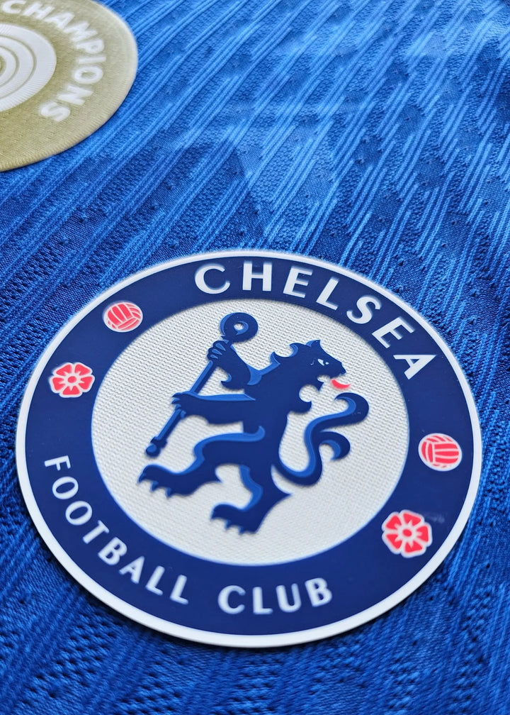 Close-up of the Chelsea Football Club crest featuring a lion and flowers on a blue background.