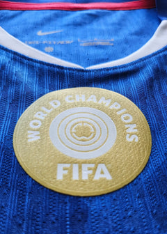 Close-up view of the FIFA World Champions badge on a blue football shirt.