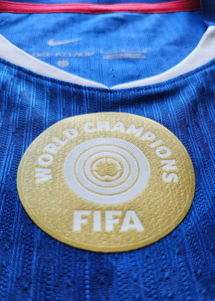 Close-up view of the FIFA World Champions badge on a blue football shirt.