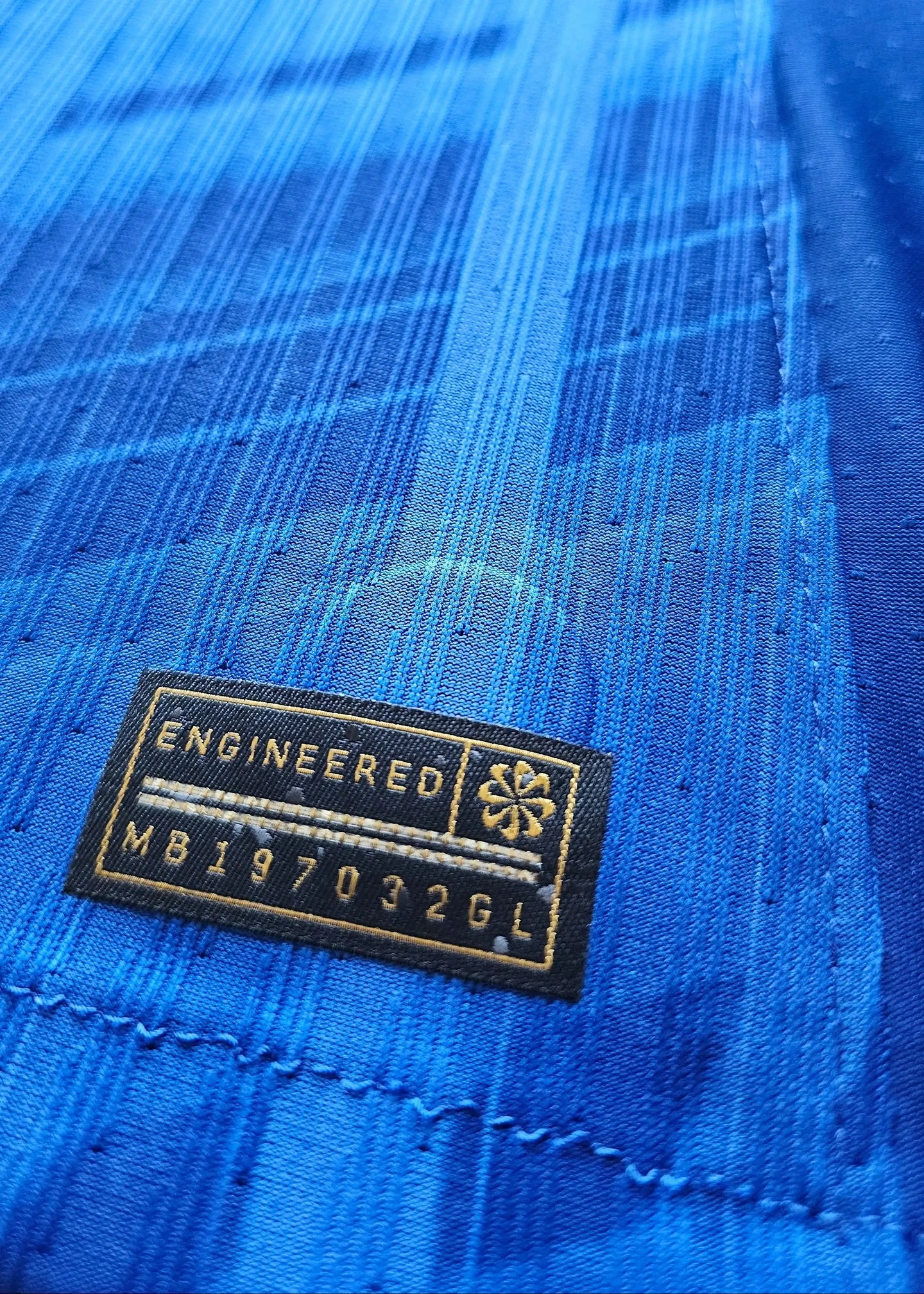 Close-up of the engineered label featuring text: ENGINEERED MB197032GL on a blue fabric background.