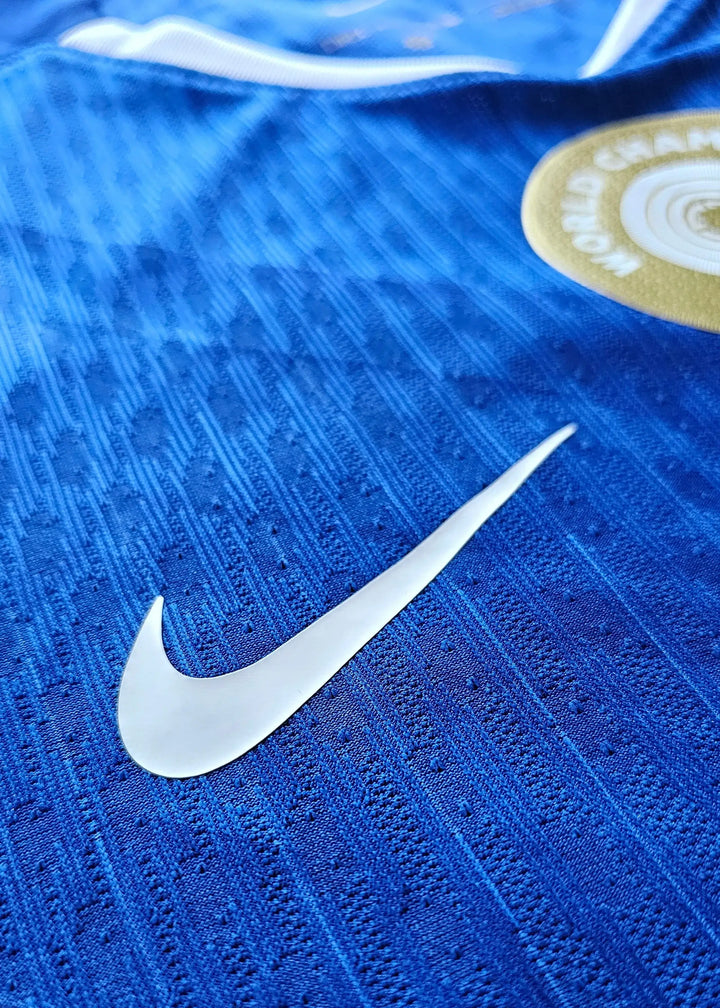 Close-up of blue fabric featuring a white Nike swoosh and circular badge with gold details.