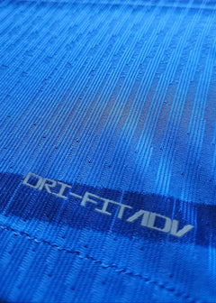 Close-up of the fabric showing textured blue pattern and 'DRI-FIT ADV' text.