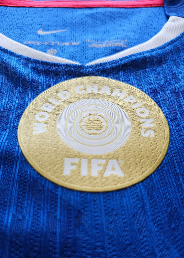 Close-up of the FIFA World Champions emblem on a blue football shirt with a Nike tag.