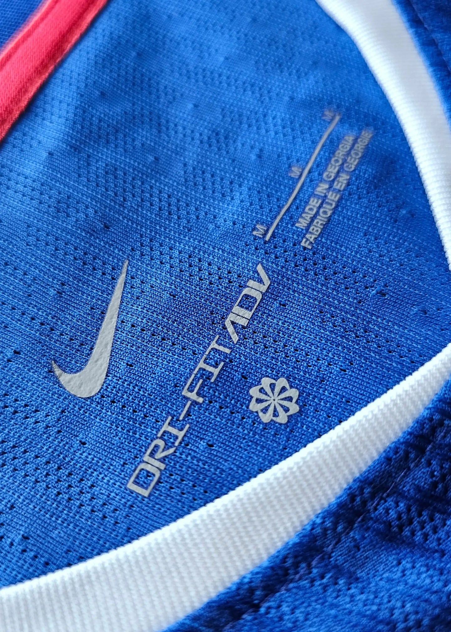 Detail showing Nike Dri-FIT ADV label and care instructions on blue fabric with white trim.