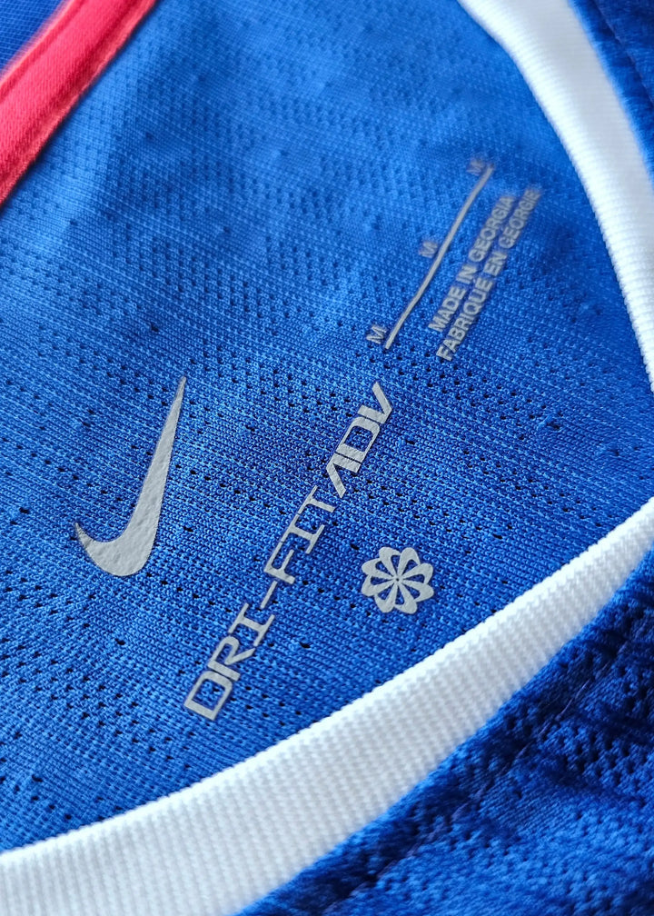 Detail showing Nike Dri-FIT ADV label and care instructions on blue fabric with white trim.