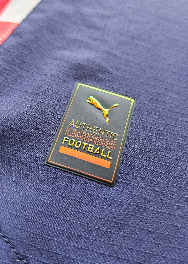 Close-up of the Puma logo with the text 'AUTHENTIC LICENSED FOOTBALL' on a navy shirt.