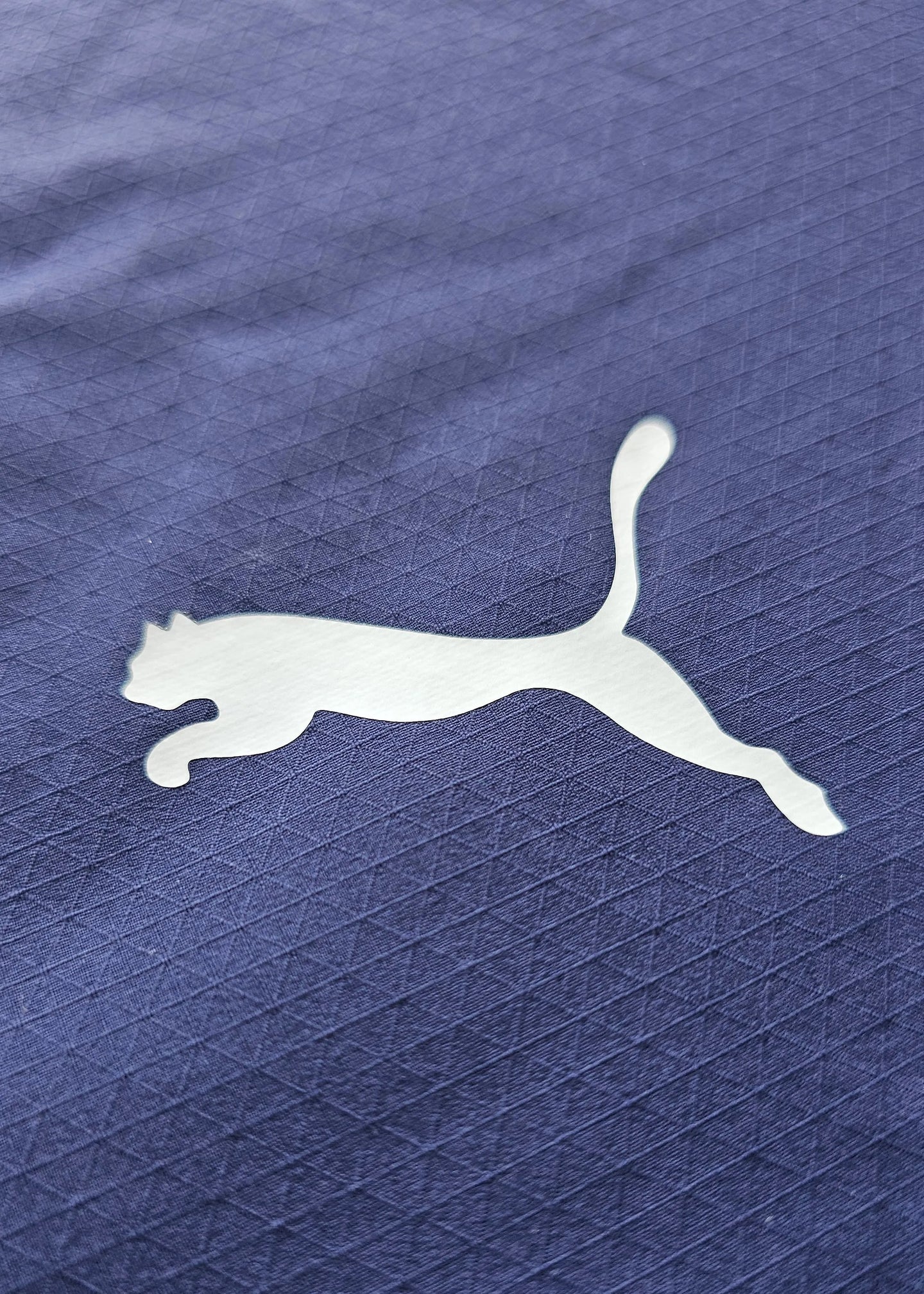 Close-up of white Puma logo on navy fabric with a textured pattern.