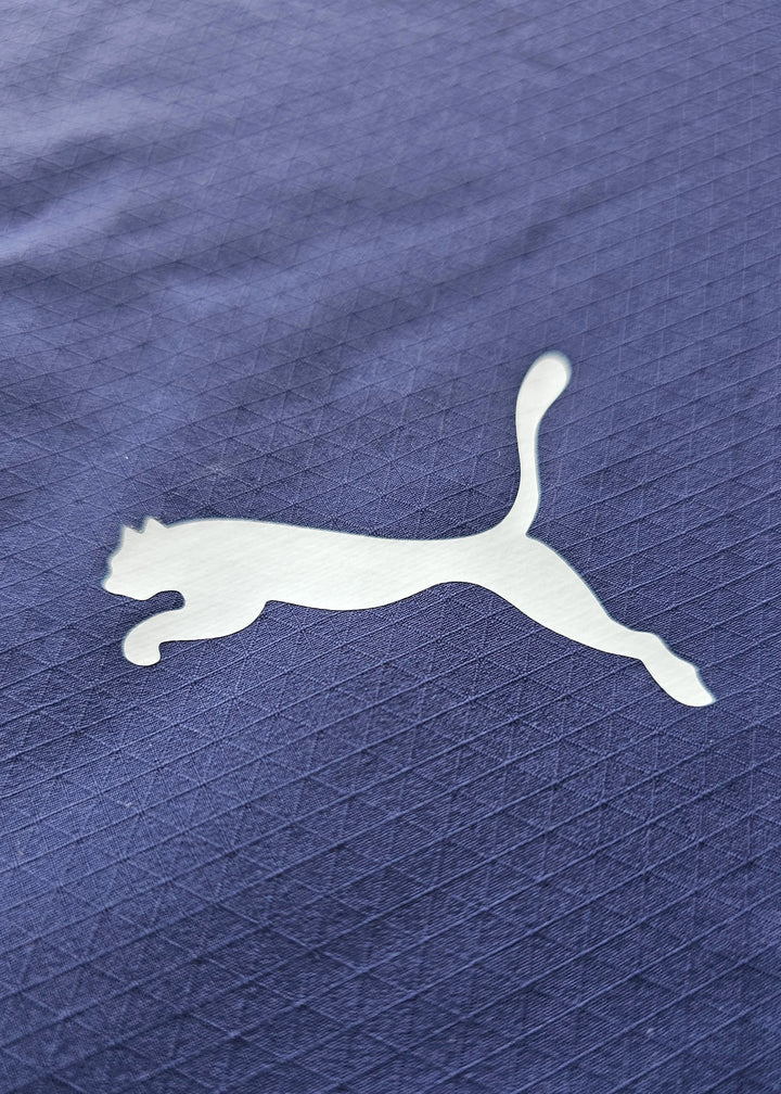 Close-up of white Puma logo on navy fabric with a textured pattern.