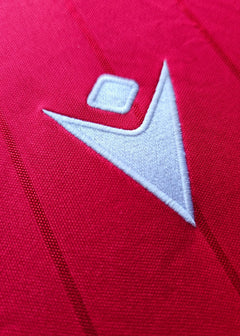 Close-up of white logo detail on red football shirt, featuring an embroidered design.