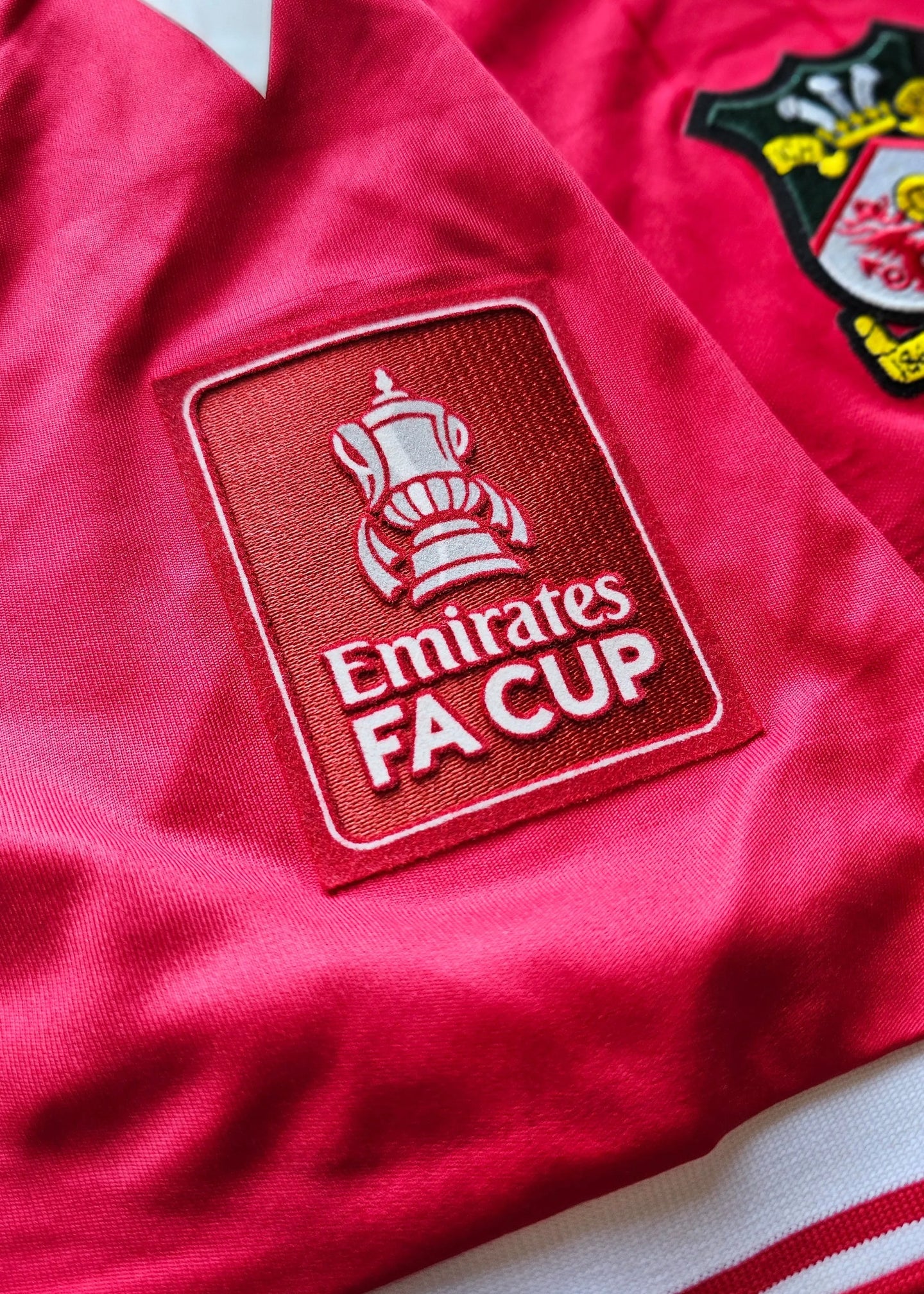 Close-up of the Emirates FA Cup badge on a red fabric with a white stripe.