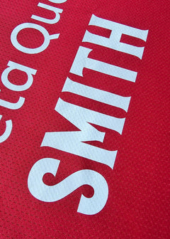Close-up of the name 'SMITH' on a red football shirt with white lettering.
