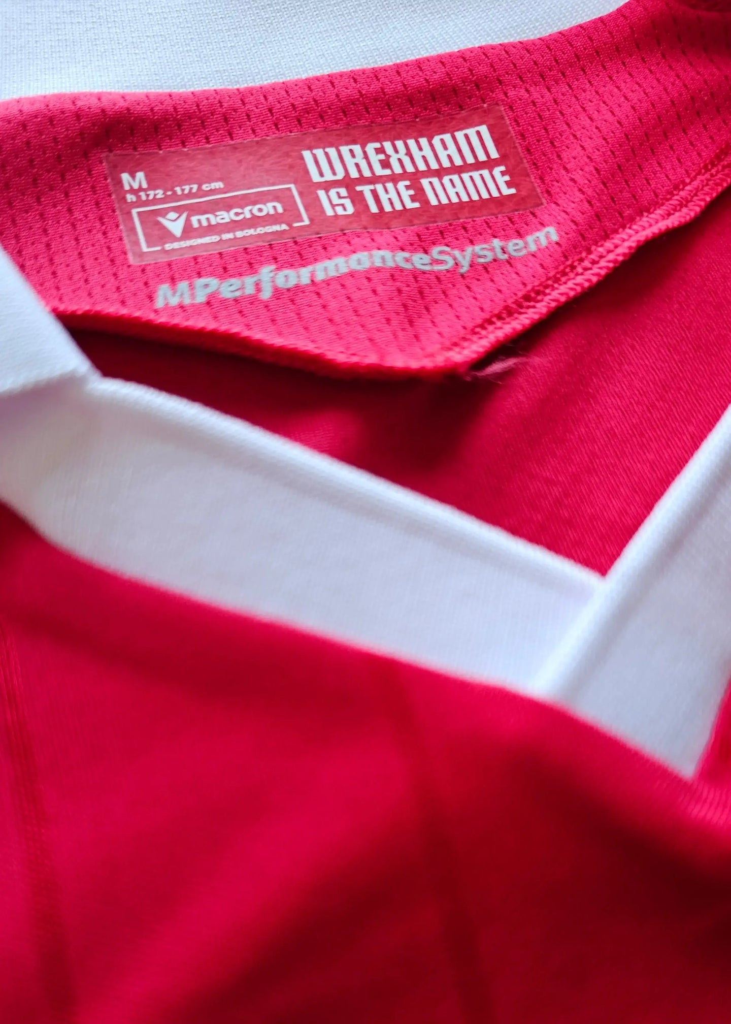 Collar detail showing 'Wrexham IS THE NAME' and Macron logo on a red football shirt.