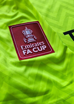 Close-up of the Emirates FA Cup patch on a bright green football shirt.
