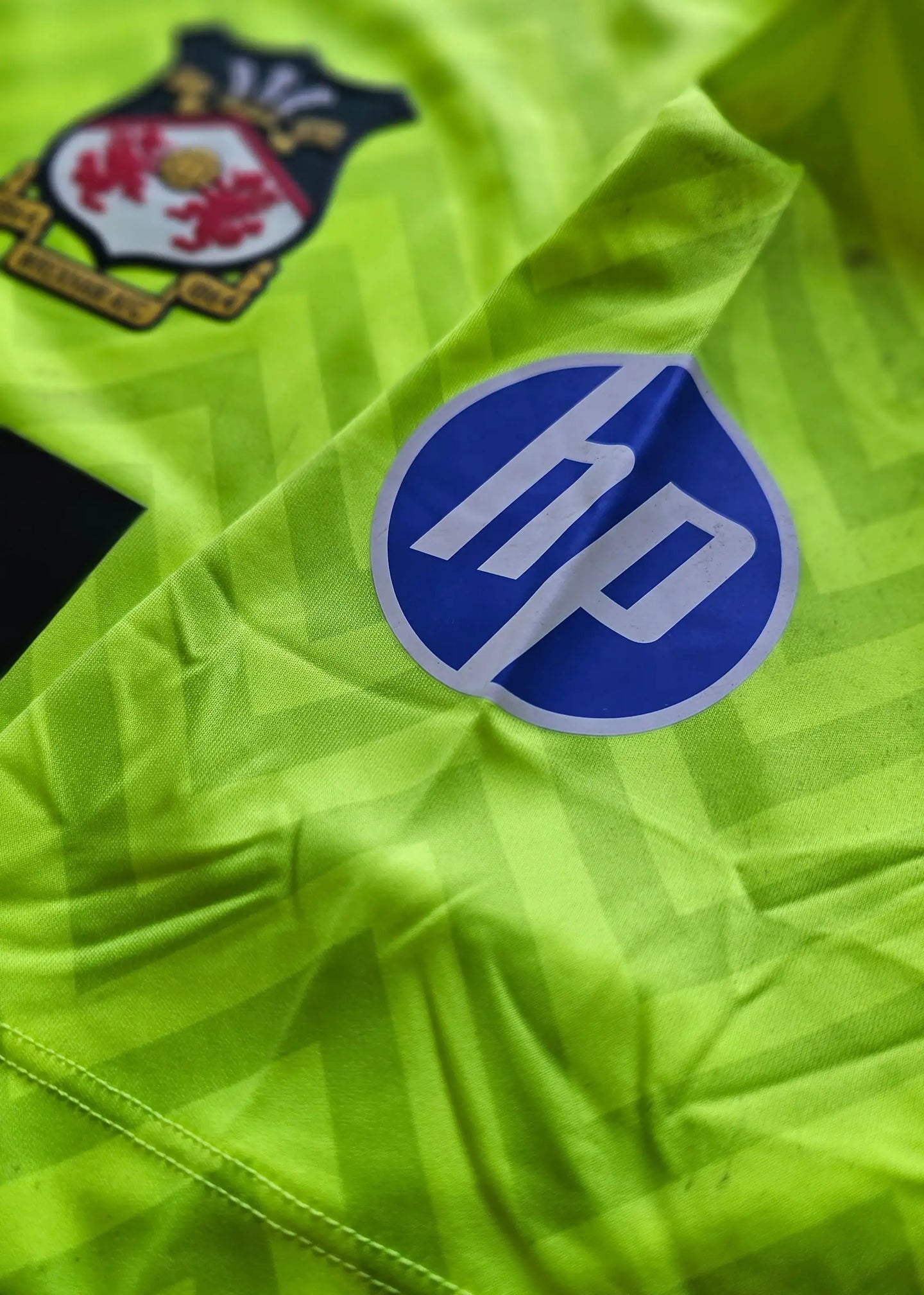 Crest of Wrexham A.F.C. and HP sponsor logo on green football shirt.