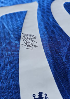 Close-up of signature on blue Chelsea F.C. football shirt, featuring texture pattern detail.