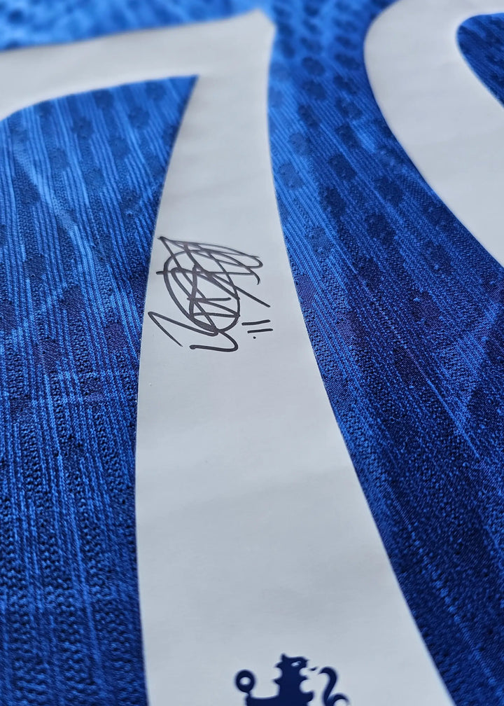 Close-up of signature on blue Chelsea F.C. football shirt, featuring texture pattern detail.