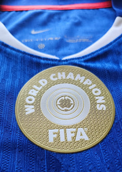 Crest detail displaying FIFA World Champions badge on blue football shirt.