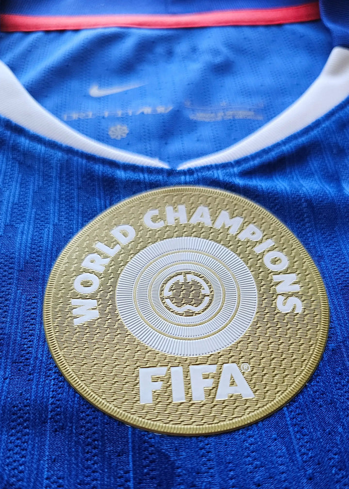 Crest detail displaying FIFA World Champions badge on blue football shirt.