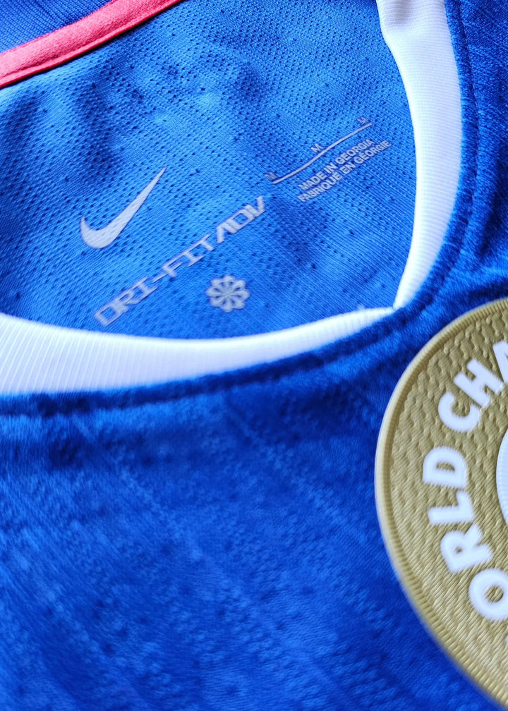 Close-up of collar with Nike logo, DRI-FIT ADV text, and gold World Champion badge on blue fabric.