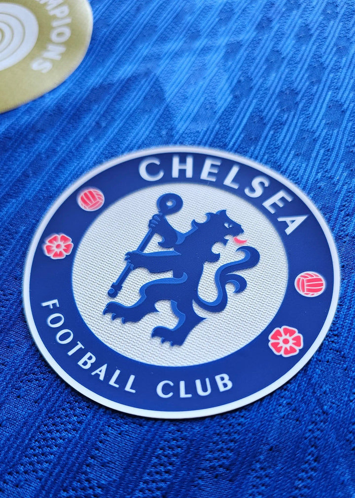 Close-up of Chelsea Football Club crest featuring a lion and flowers on a blue background.