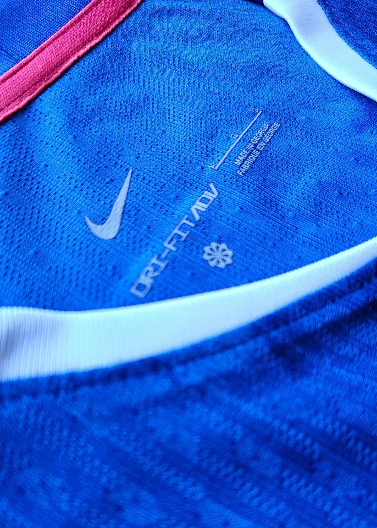 Detail view showing Nike DRI-FIT ADV label on a blue football shirt with pink trim.