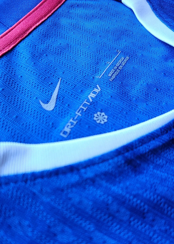 Detail view showing Nike DRI-FIT ADV label on a blue football shirt with pink trim.
