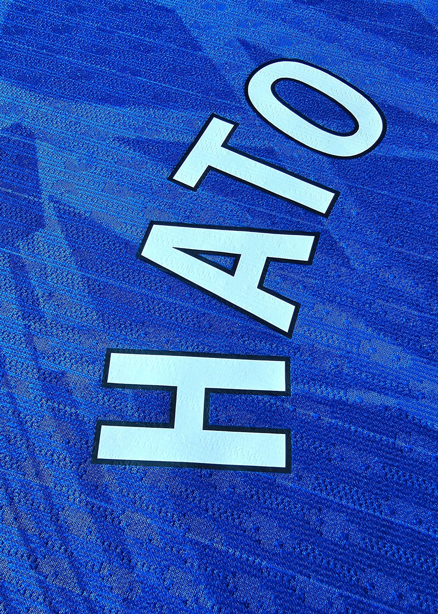 Close-up view of the name 'HATO' in white lettering on a blue football shirt.