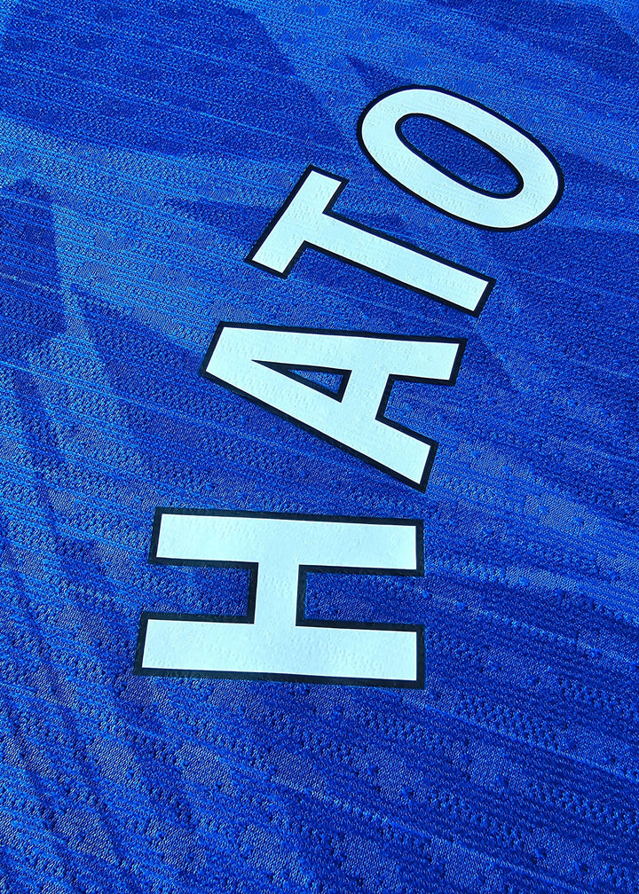 Close-up view of the name 'HATO' in white lettering on a blue football shirt.