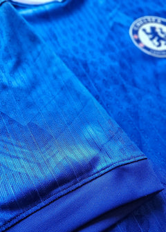 Detail of blue Chelsea F.C. football shirt showing the badge and fabric texture.
