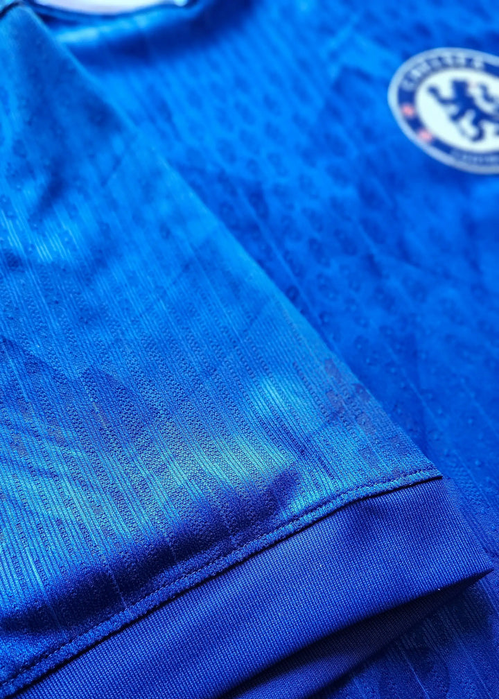 Detail of blue Chelsea F.C. football shirt showing the badge and fabric texture.