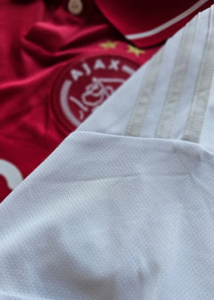 Close-up of the red AFC Ajax crest with two stars and white striped fabric detail.