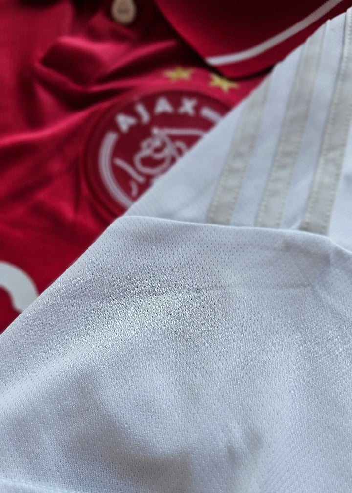 Close-up of the red AFC Ajax crest with two stars and white striped fabric detail.