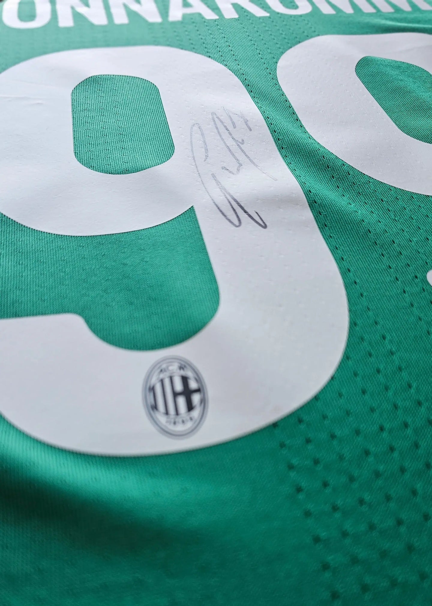 Close-up of No. 99 with signature and AC Milan crest visible on green football shirt.