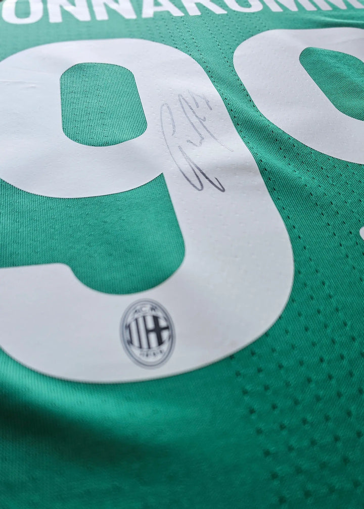 Close-up of No. 99 with signature and AC Milan crest visible on green football shirt.