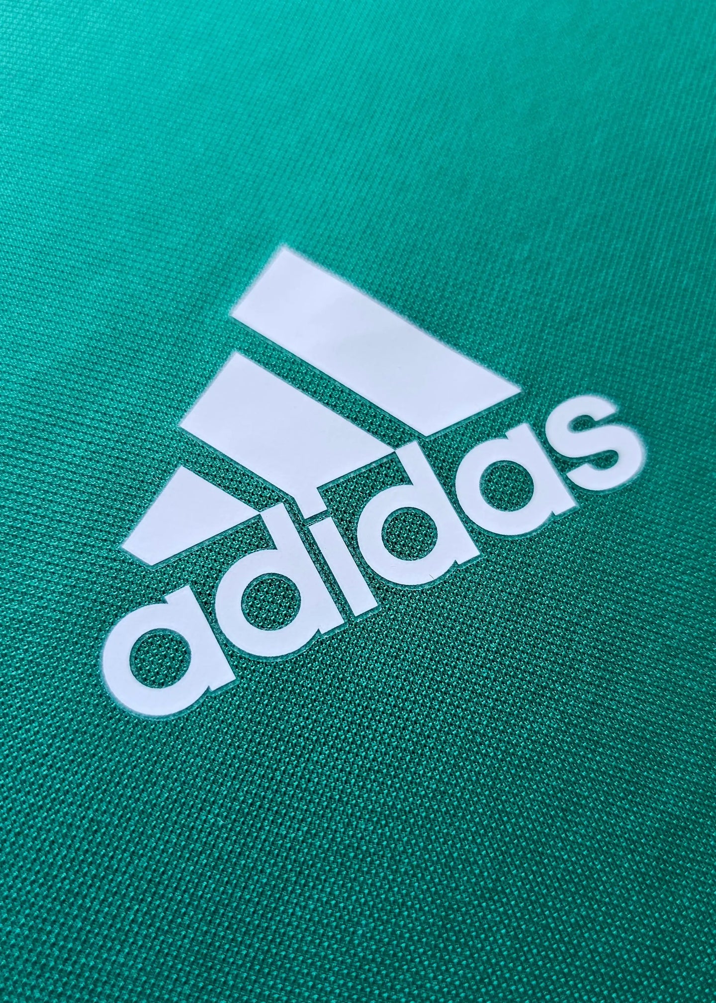Close-up of white adidas logo on green fabric detailing the Signed Gianluigi Donnarumma jersey.